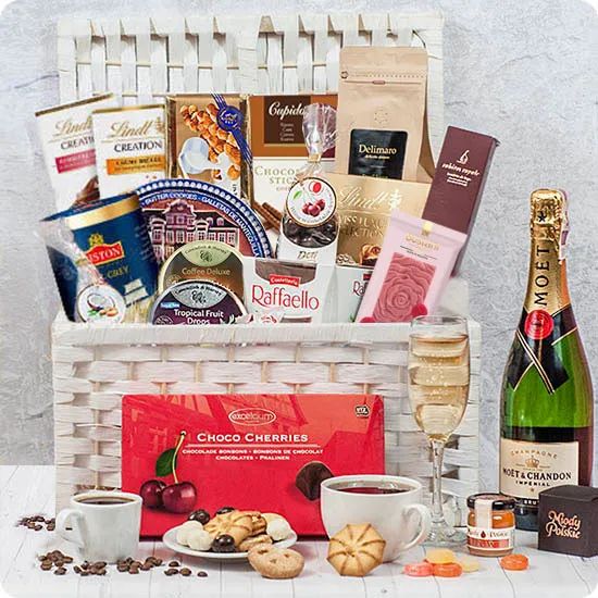 biały kosz wiklinowy wypełniony słodyczami, szampanem MOET, kawą i herbatą